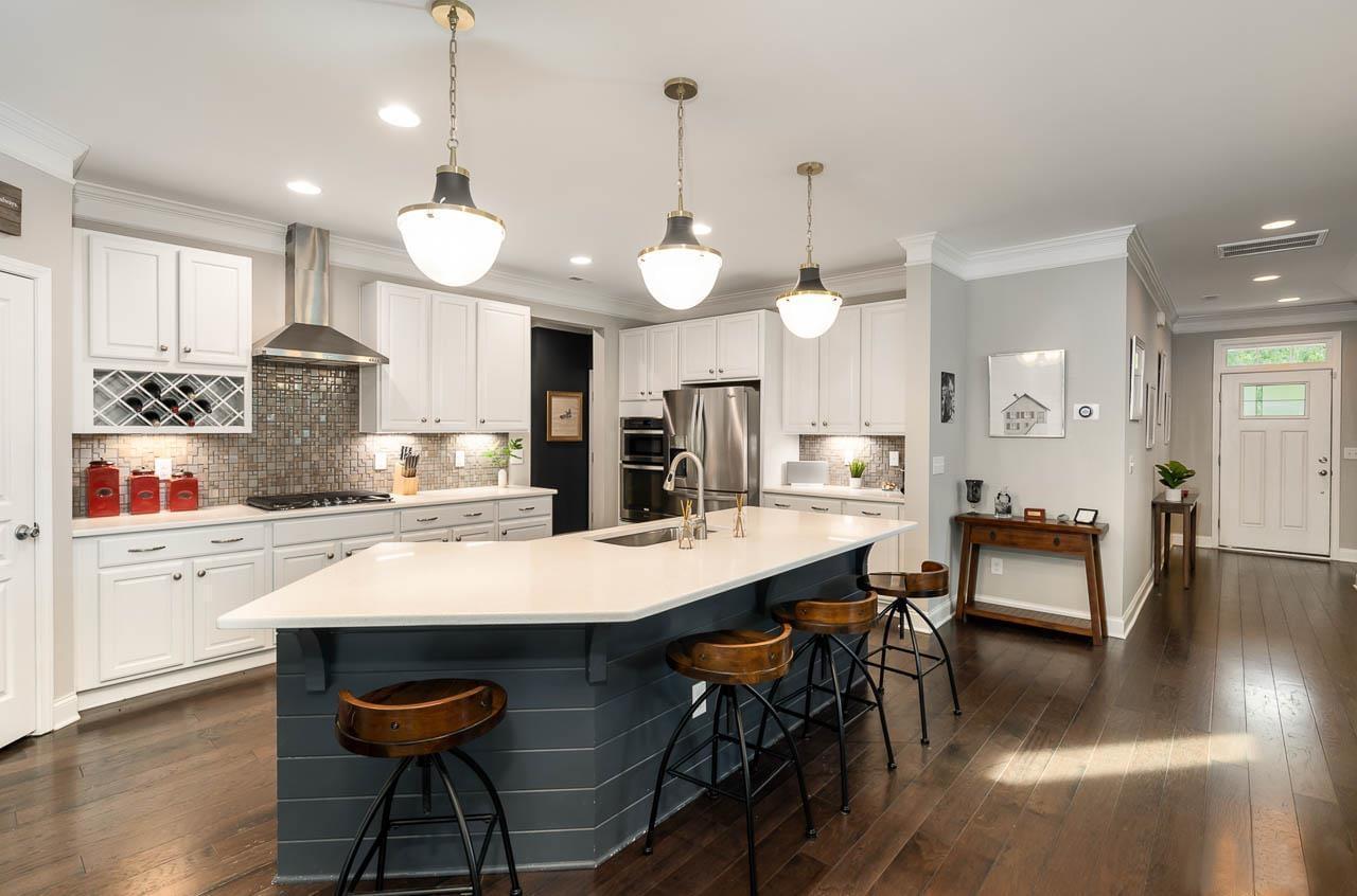 A spacious kitchen with a blue gray kitche island, white countertops, sparkly backsplash, and tons of light